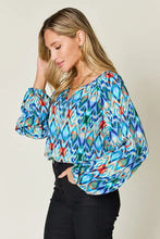 A vibrant double take full size printed balloon sleeve blouse with long sleeves and bold blue green ikat pattern with red accents