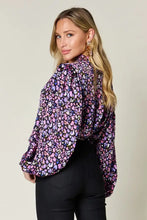 A woman wearing a double take full size printed balloon sleeve shirt with vibrant pink purple floral pattern and jeans size fit