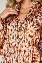 A women’s long-sleeved blouse with warm-toned leopard print, ruffled cuffs and neckline, and wooden buttons