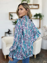 A woman wears a double take full size printed smocked long sleeve blouse with a teal and purple abstract pattern on lightweight fabric