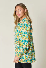 A woman wearing a double take full size printed smocked long sleeve blouse with teal yellow and white wave patterns