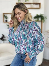 A woman wears a double take full size printed smocked long sleeve blouse with teal and purple floral lightweight fabric