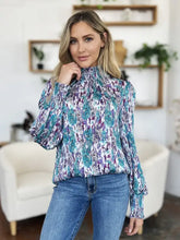 A woman wearing a double take full size printed smocked long sleeve blouse with teal and purple abstract pattern