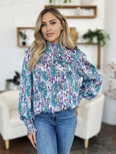 A woman wears a double take full size printed smocked long sleeve blouse with teal and purple abstract pattern