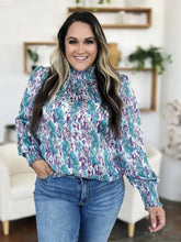 A plus-size woman wearing a double take full size printed smocked long sleeve blouse in teal and purple lightweight fabric