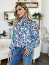 A woman wears a double take full size printed smocked long sleeve blouse in teal and purple lightweight fabric