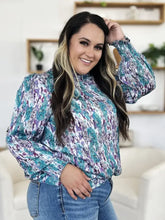 A plus-size woman wears a teal purple and white patterned double take full size printed smocked long sleeve blouse