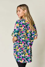 Double take full size printed v-neck short sleeve side slit top in vibrant purple green yellow and pink floral pattern ideal for jeans size pairing