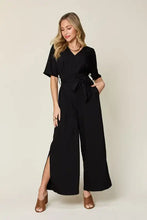 Black v-neck jumpsuit with 3/4 sleeves, belted waist, wide-leg pants, side slit, machine wash cold