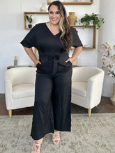 Black satin v-neck jumpsuit with flutter sleeves, tie belt and side slit, machine wash cold