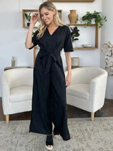 Black v-neck jumpsuit with short sleeves, tied waistband, and side slit. Machine wash cold
