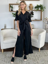 Black satin-like v-neck jumpsuit with flutter sleeves, tie belt, side slit, machine wash cold