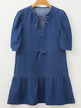 A blue denim mini dress with puff sleeves, tie-front neckline, and a high waist tiered skirt design