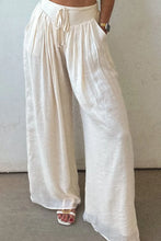 Cream-colored tie waist pleated wide leg pants in lightweight textured fabric with elastic waistband and drawstring
