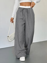 High-waisted striped wide leg pants with black and white vertical pinstripes and a wide leg drawstring waistband