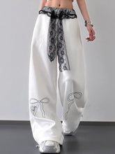 White wide leg pants with black lace belt detail and delicate bow embroidery on the lower legs
