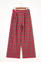 Red plaid wide-leg pants with black and white striped plaid pattern hanging on a wooden hanger