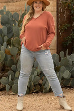 Rust notched long sleeve V-neck top with distressed denim jeans and white cowboy boots