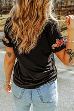 Woman in embroidered round neck tee shirt and light-wash jeans from behind