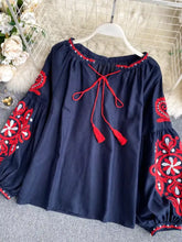 Navy blue long-sleeved embroidered tassel tie neck blouse with red and white floral embroidery on sleeves neckline and hem