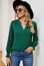 Woman in notched lantern sleeve T-shirt, dark green V-neck top, jeans, hat, sunglasses