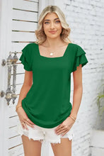 Woman in emerald green square neck flutter sleeve top and white denim shorts