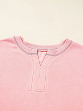 A soft pink ribbed-knit top with a v-shaped neckline and gray stitching featuring color block patchwork details