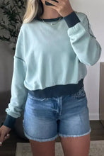 Light blue exposed seam cropped sweatshirt with dark navy ribbed cuffs made of slightly stretchy material, machine wash cold