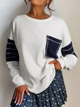 White long-sleeved sweatshirt with navy contrast panels and stitched pocket featuring exposed seam detail, machine wash cold