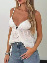 White eyelet lace trim cami with delicate floral patterns and a black bow at the center for elegant wear