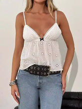 White eyelet lace trim cami with delicate floral cutouts and small black bow at center for elegant layering