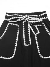 Black high-waisted wide leg trousers with white crochet trim tie and scalloped crochet trim along pockets and waistband