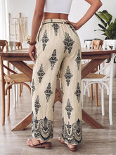 Cream-colored boho print wide leg pants with black ornate floral and lace patterns along the legs and hem