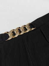 Gold-toned chain waist belt clip attached to black pleated fabric of plus size chain-waist wide-leg pants with care instructions for machine wash