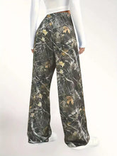 Relaxed fit camo print wide-leg pants with drawstring waist featuring dark green brown and tan leaf camouflage pattern