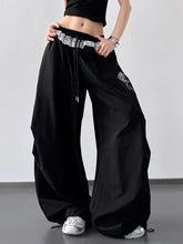 Black wide leg pants featuring drawstring lace trim at the waistband and subtle embroidered rose on the thigh