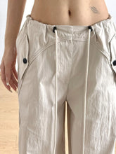Beige relaxed wide-leg drawstring pants with black button accents and a tapered fit in lightweight fabric