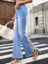 Light blue denim floral embroidered flare jeans with colorful floral embroidery and frayed hem along the outer leg