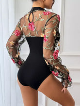 Black long sleeve bodysuit with sheer mesh long sleeve and embroidered pink and peach roses on floral mesh background