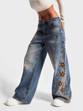 Blue denim wide leg jeans featuring orange floral embroidery along the outer leg in a floral embroidered wide style