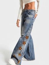 Blue denim wide leg jeans with orange floral embroidery along the outer leg in a floral embroidered wide style