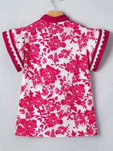 A white blouse with vibrant fuchsia floral print and lace-trimmed flutter sleeves on a wooden hanger