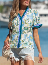 A woman wearing a light blue and green floral print short sleeve blouse with ruffled sleeves and striped trim