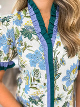 White short sleeve blouse with vibrant blue and green floral print and ruffled teal and lavender striped trim