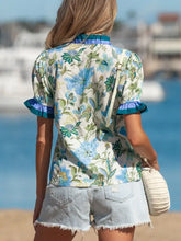 A woman wears a short sleeve blouse with floral print and striped trim featuring blue green blossoms on off-white fabric