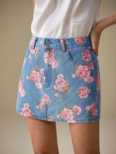 A denim mini skirt in light blue with a vibrant pink rose floral print featuring floral print denim design