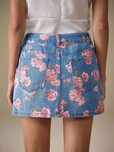 A light blue denim skirt with a vibrant pink rose floral print featuring classic back pockets and tailored waistband