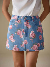 A denim skirt with a vibrant pink rose floral print on medium-wash blue fabric featuring floral print denim design