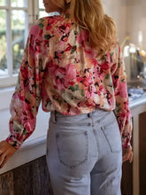 A woman wearing a floral print frill trim shirt with vibrant pink and peach floral patterns on sheer satin fabric