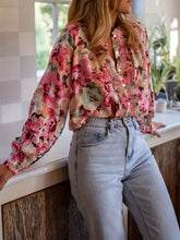 A woman wears a long-sleeved floral print frill trim blouse in vibrant pink sheer flowing fabric